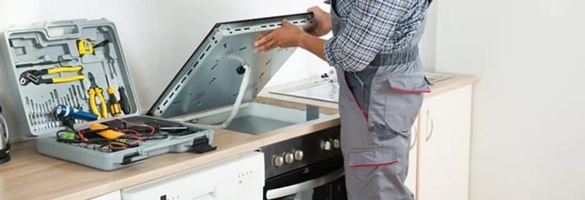 Cooktop repair technician lifting a built-in stovetop for service in Memphis, TN