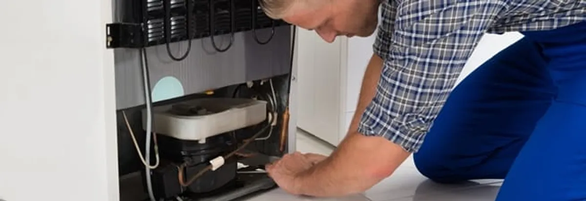 Refrigerator repair technician servicing the compressor and condenser area in Memphis, TN